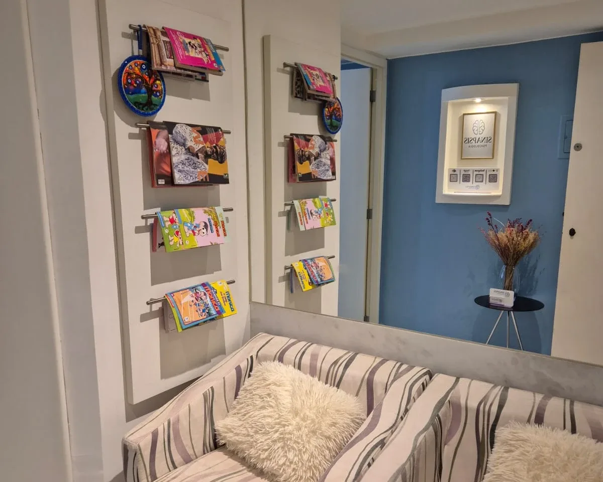 Espaço de espera infantil da Clínica SINApsis, com revistas e livros infantis ao alcance das crianças.